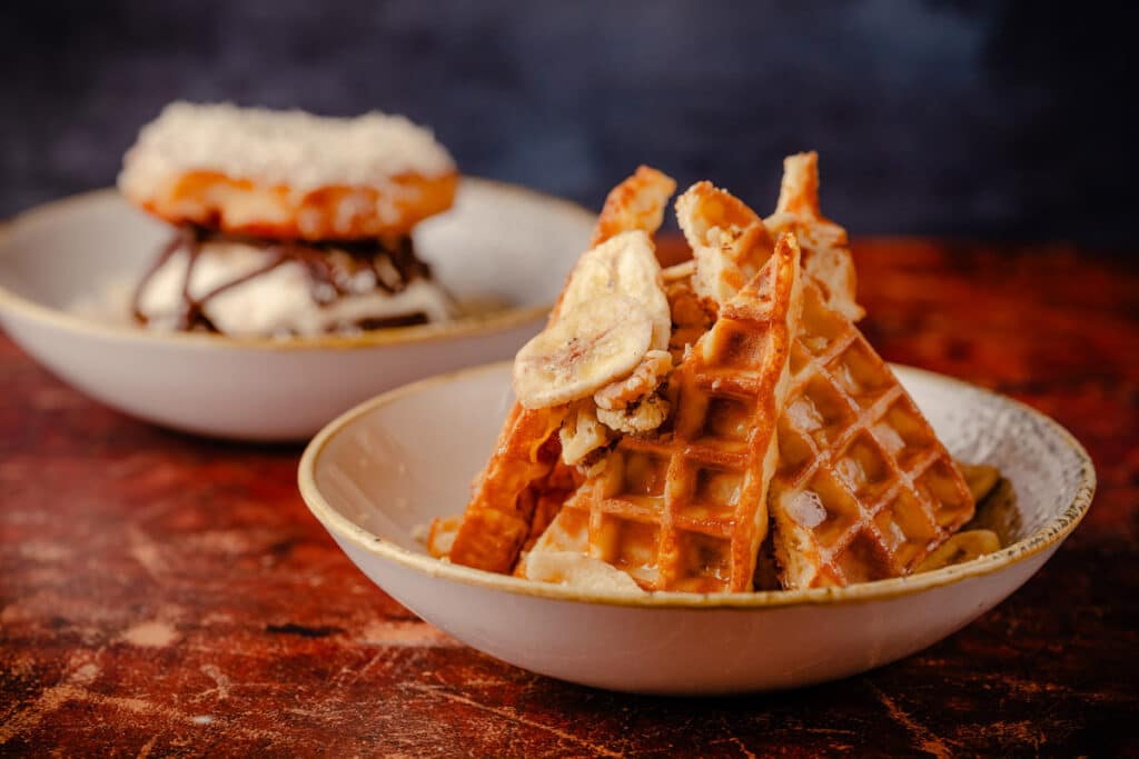 RC3-January25-FullAlbum-59 Waffles with bananas and walnuts, carefully cut into diagonals and arranged upright in the center of a bowl.